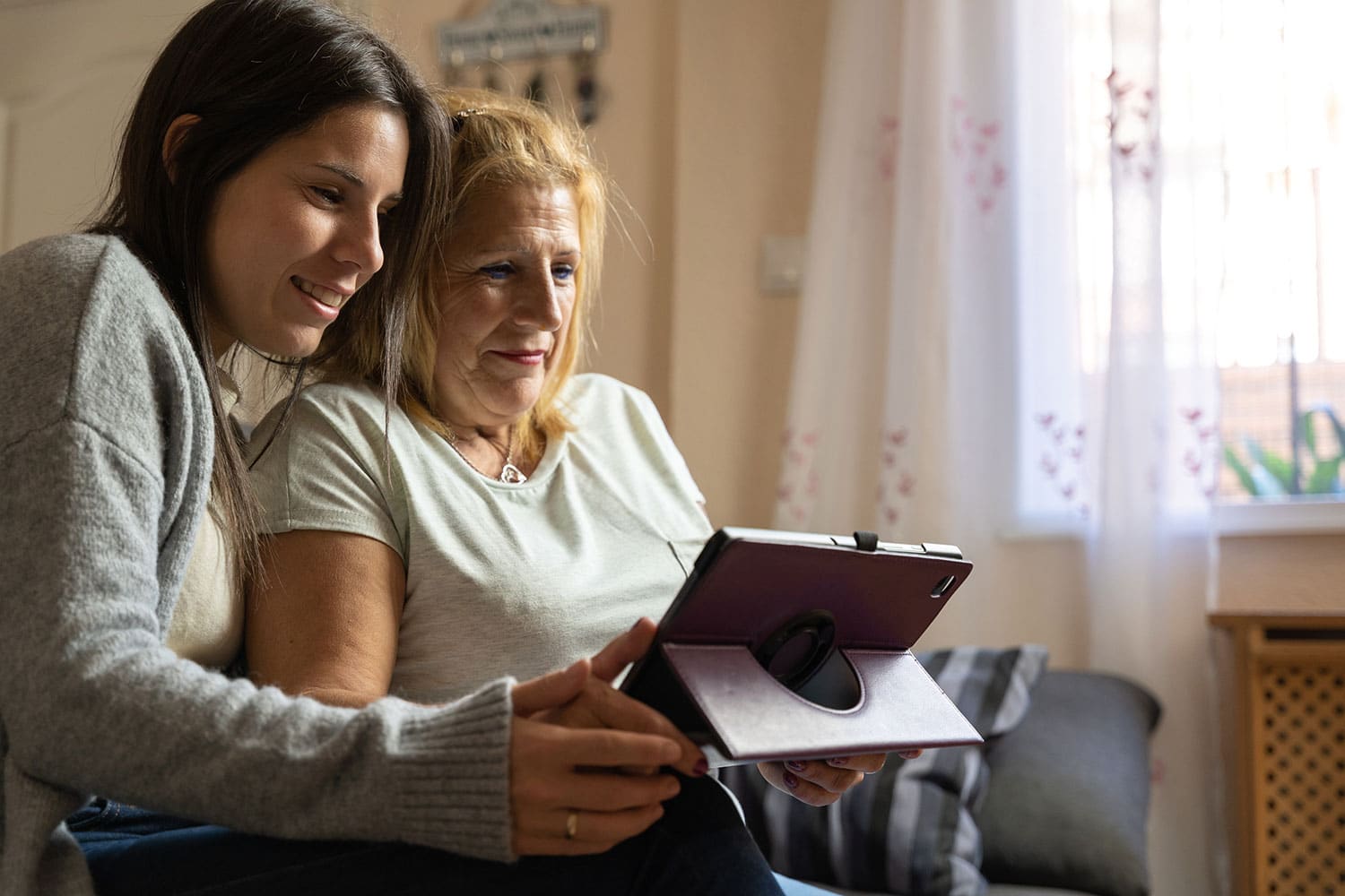 mother and daughter reading tablet and smiling, selecting memory care